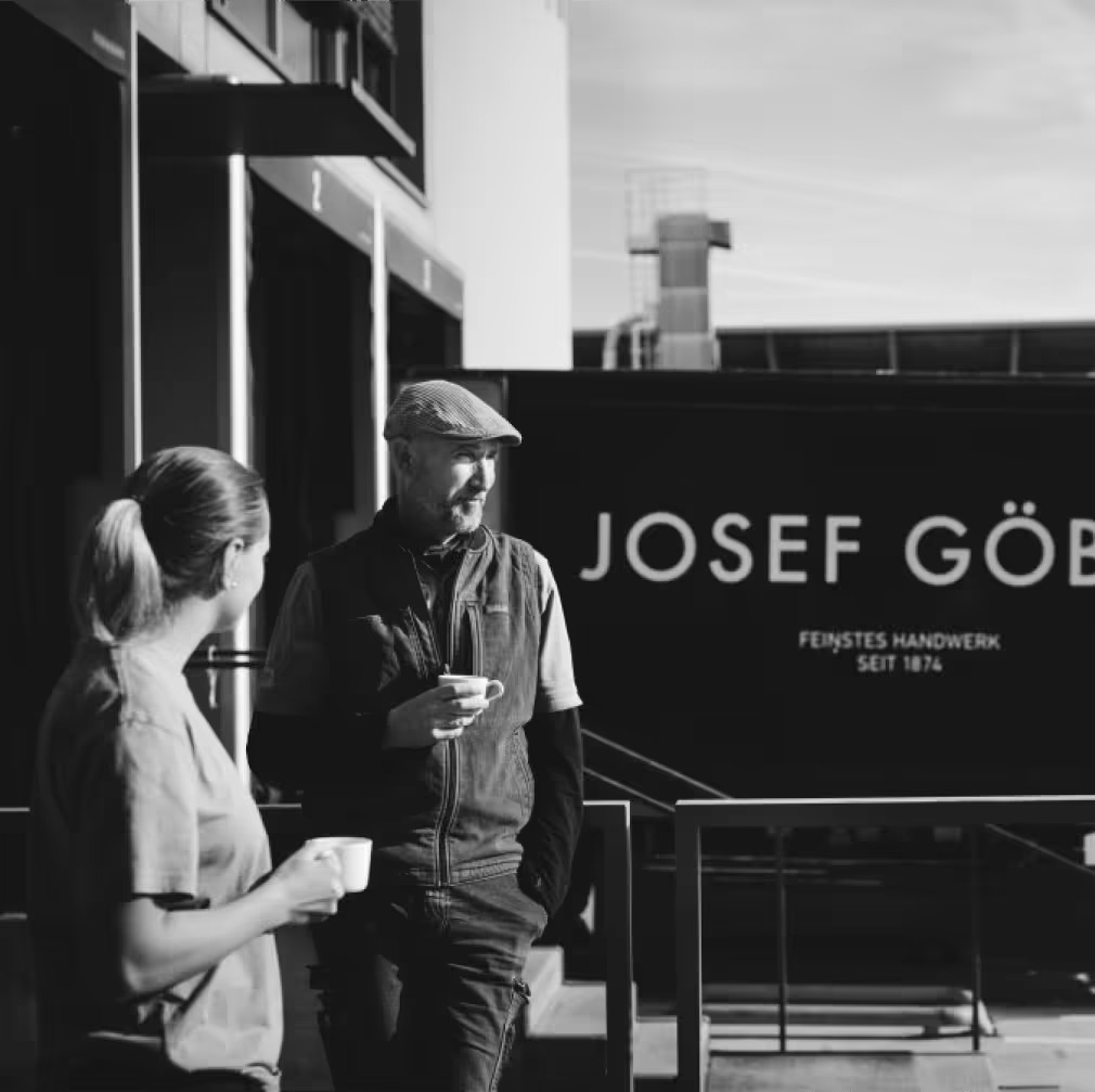 Ein Mann und eine Frau stehen vor einem Gebäude mit einem Schild, auf dem Josef Göbel steht.