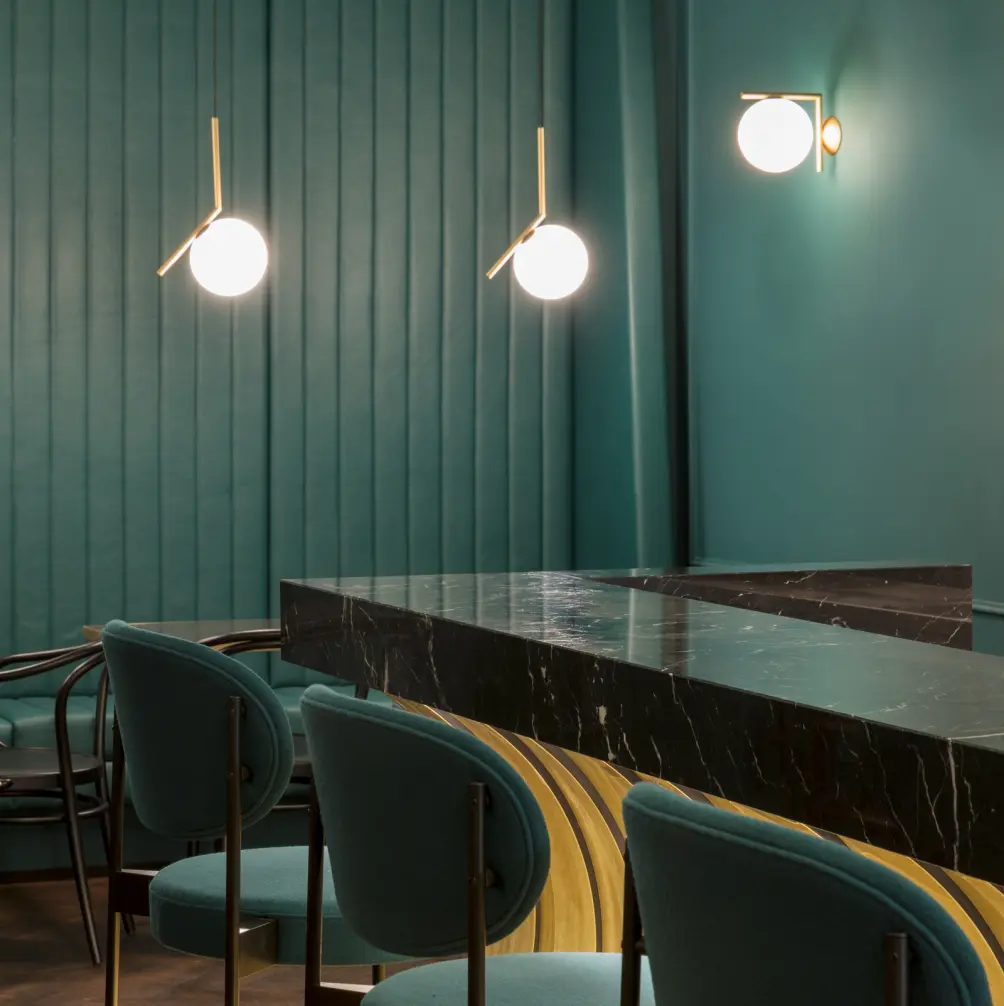 Eleganter Barbereich mit dunklem Marmortresen, samtbezogenen Stühlen in Petrol, goldenen Akzenten und modernen Wand- und Pendelleuchten
